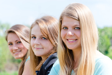 Obraz premium Three happy teen girls looking down against blue sky