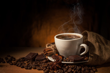 Cup of coffee in coffee beans on brown background