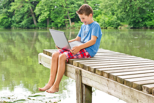 Lachender Jugendlicher mit Notebook am idyllischen Teich