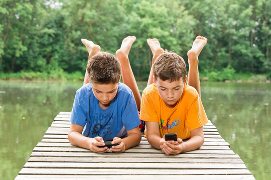 Zwei jugendliche Freunde mit Smartphone am idyllischen Teich