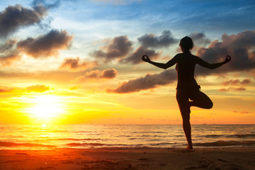 Fototapeta na wymiar Woman practicing yoga on the beach, during sunset.