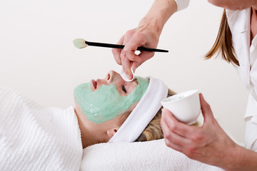 Beautician retouching a blond woman thalasso facial mask. - obrazy, fototapety, plakaty