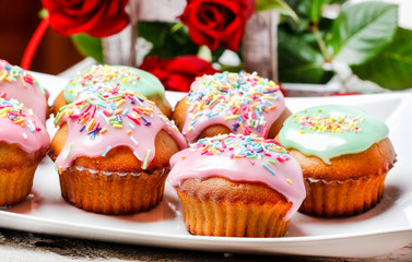 Muffins covered with pink icing and colorful sprinkles on wooden