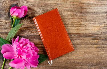 Small book and lush pink peonies on wooden table. Top view, copy