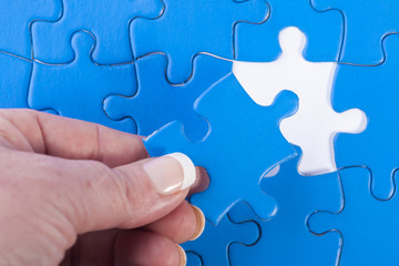 Woman's hand placing missing piece in Jigsaw puzzle  signifying