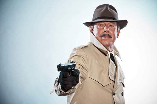 Retro detective with mustache and hat. Holding gun. Studio shot.