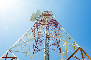 communications tower showing sun flare with antennas against blu