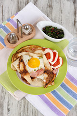 Scrambled eggs and pancake on plate on napkin on wooden table