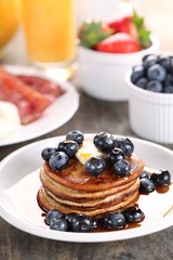Pancakes, fresh fruits, juice and eggs with bacon.