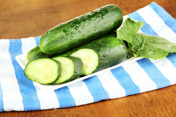 Tasty green cucumbers on color napkin, on wooden background