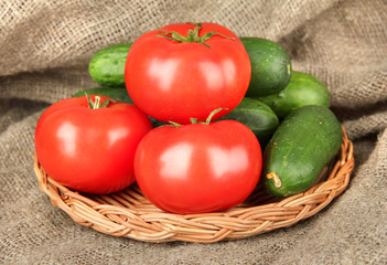 Tasty green cucumbers and red tomatoes on sackcloth background