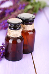 Medicine bottles and salvia flowers on purple wooden background