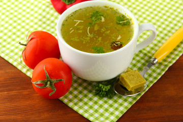 Cup of soup with bouillon cubes on wooden background