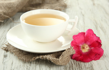 Cup of tea and pink mallow flower on wooden background