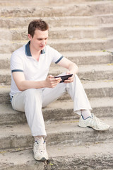 Obraz premium Young man sitting on a stairs with tablet pc