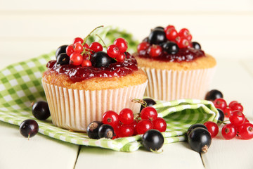 Tasty muffins with berries on white wooden table