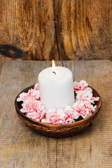White candle among carnation flowers in vintage wooden bowl