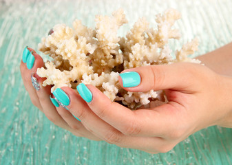 Beautiful woman hands with blue manicure holding coral,