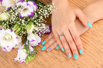 Beautiful woman hands with blue manicure near bouquet of