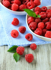 Ripe sweet raspberries in bowls on wooden background