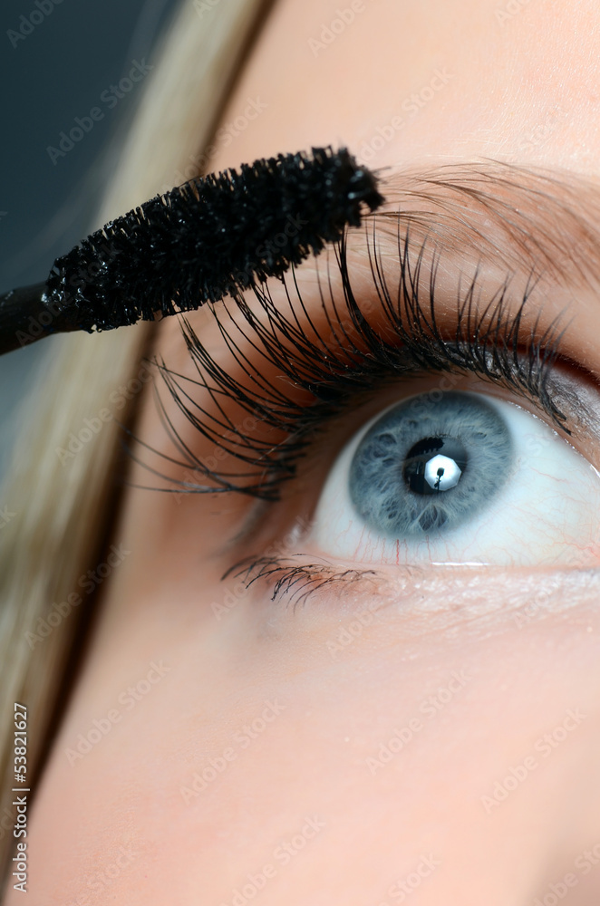 Wall mural Woman applying mascara on her eyelashes - macro shot