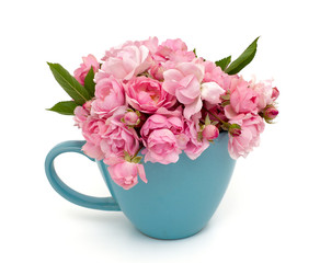 blue cup full of small pink roses over white