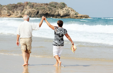 Happy senior couple walking together on a beach - 53842048