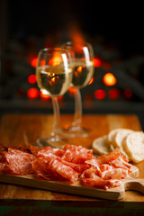 Platter of serrano jamon Cured Meat with cozy fireplace and wine