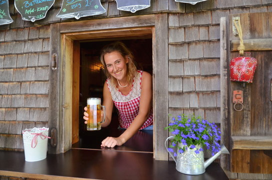 Junge Frau im Dirndl serviert Bier auf Bergh&uuml;tte in den Alpen, Bayern