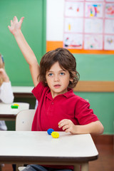 Boy With Hand Raised Sitting At Desk