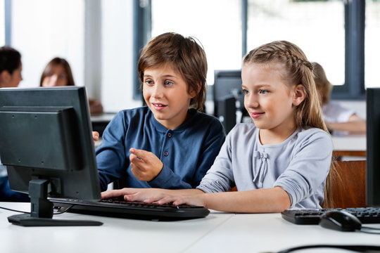 Boy Pointing While Using Desktop Pc With Friend At Desk