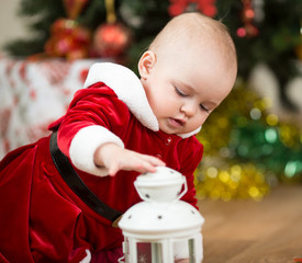 kid girl dressed as Santa Claus in front of Christmas tree with