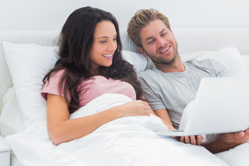 Fototapeta premium Couple in bed looking at their laptop