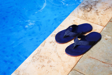 pair of blue flip flops at the edge of a swimming pool