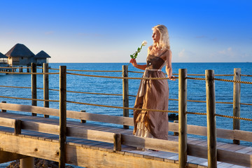 young beautiful woman in long dress on wooden road over ea..