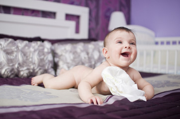 Baby vs diapers. Lying on parents bed.