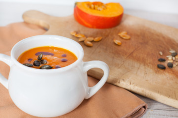 Pumpkin vegetable cream soup in white bowl with piece pumpkin