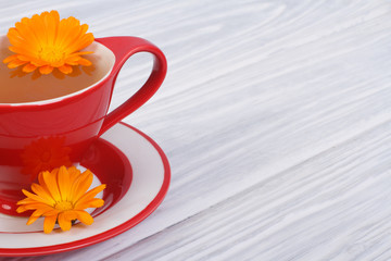 herbal tea with calendula flowers in a red cup on the table