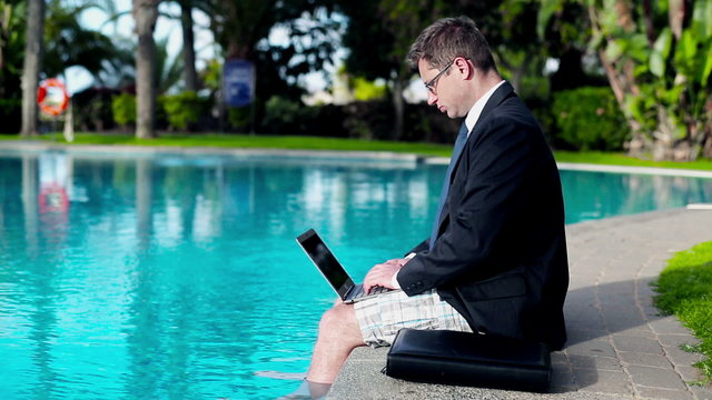 Businessman working with laptop on his vacation by the swimming 
