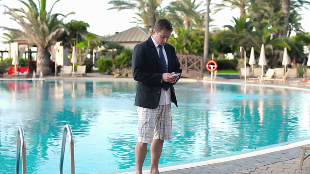 Businessman with cellphone on his vacation walking by swimming p