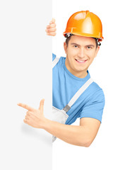 Young smiling construction worker with helmet pointing on a pane