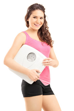 Smiling female athlete holding a weight scale and looking at cam