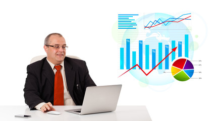 Businessman sitting at desk with laptop and statistics