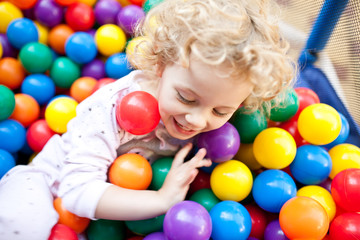 Fototapeta na wymiar A young blond girl child having fun playing with сolorful balls