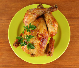 Roasted whole chicken on a green plate on wooden background