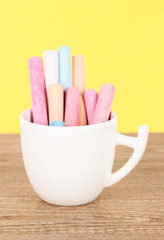 Colorful chalks in cup on table on yellow background