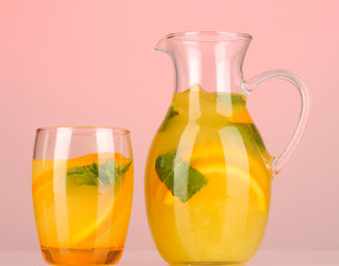 Orange lemonade in pitcher and glass on pink background