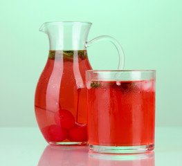 Cherry drink in pitcher and glass on green background.