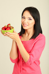 Beautiful young woman with strawberries on grey background