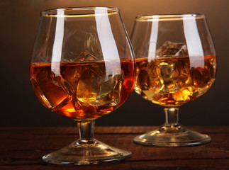 Brandy glasses with ice on wooden table on brown background